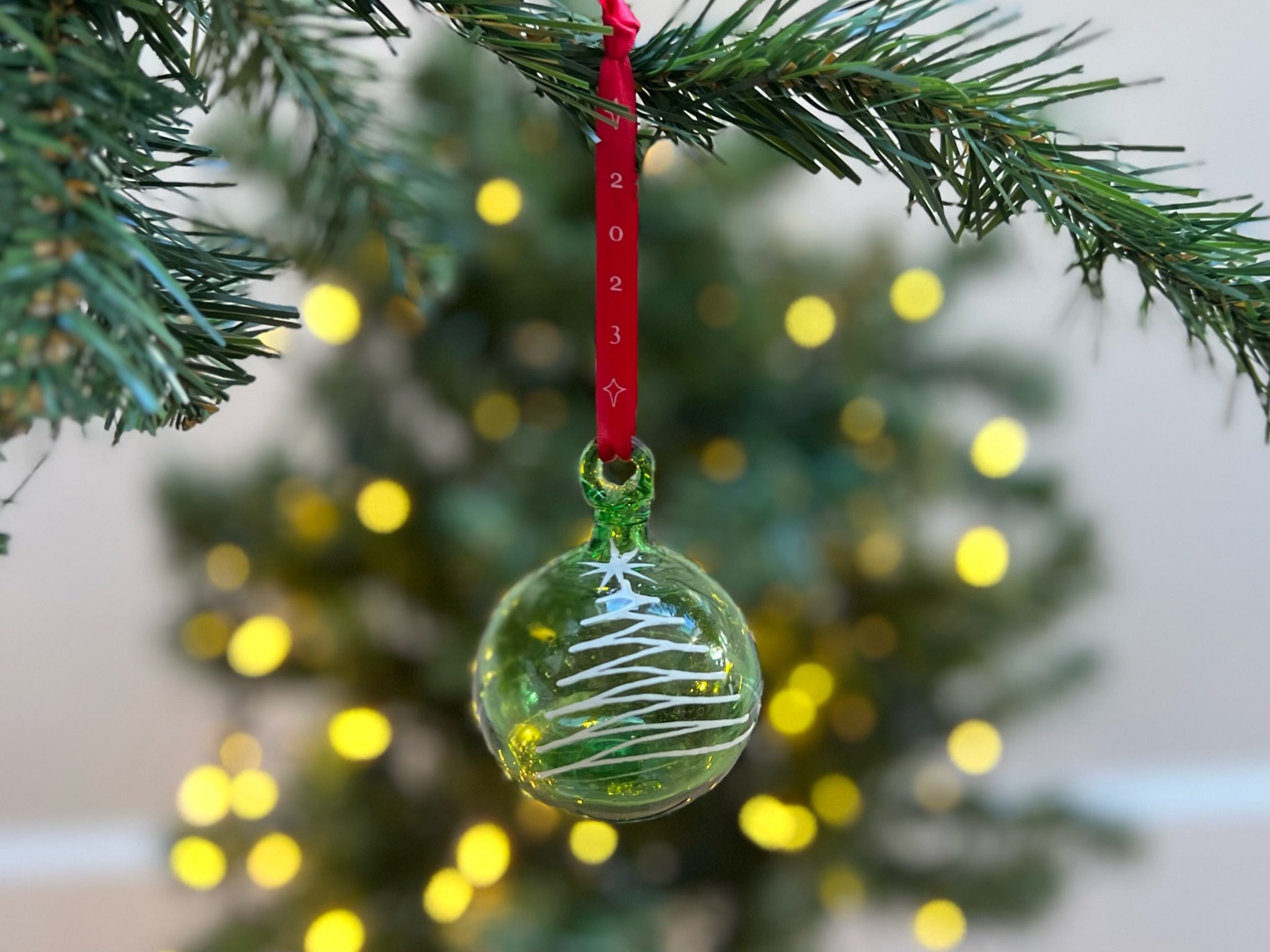 Green glass Christmas ornament painted with white tree on red ribbon